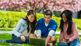 three students sitting on the green with a laptop