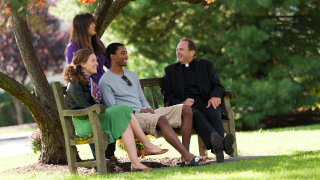 Students with a priest on campus. 