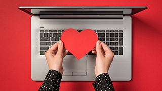 Laptop with a person holding a heart over the keyboard.