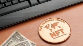 Image of a NFT coin and two US dollars next to a keyboard on a desk.