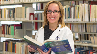 nursing grad student in the library, smiling and holding a book