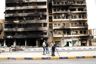 People walking in front of a war torn building.