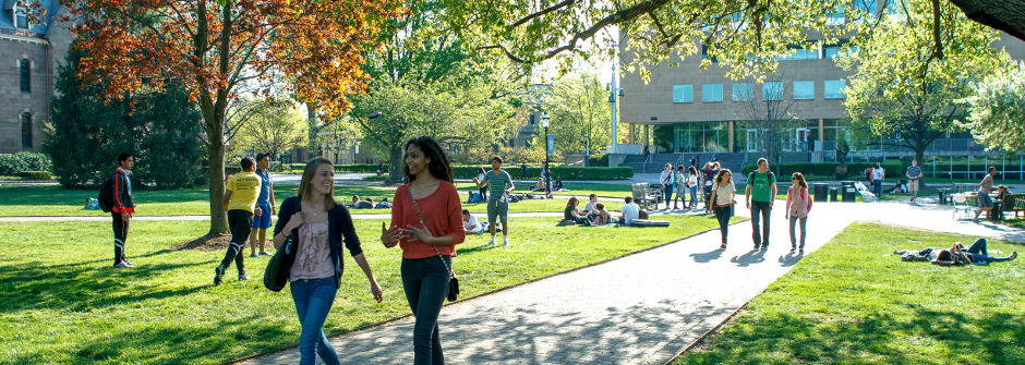 Groups of students talking and walking on the green.