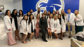 A group of nursing students wearing white coats with Professor Linda Ulak.
